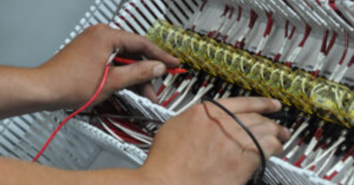 Technician testing electrical connections with a multimeter in an industrial wiring panel.</p>
<p>