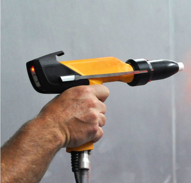 Worker using a Gema powder coating spray gun to apply red powder coating to a small metal part.