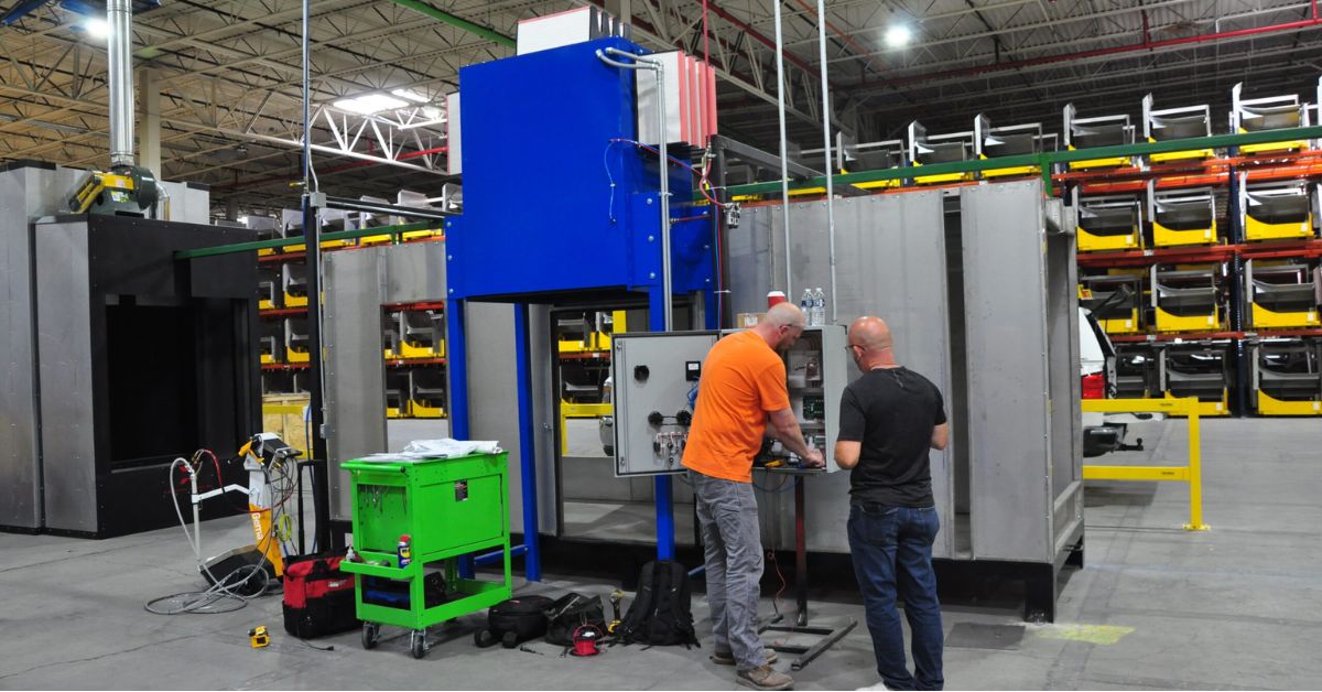 Two technicians working on an industrial powder coating system in a manufacturing facility.

